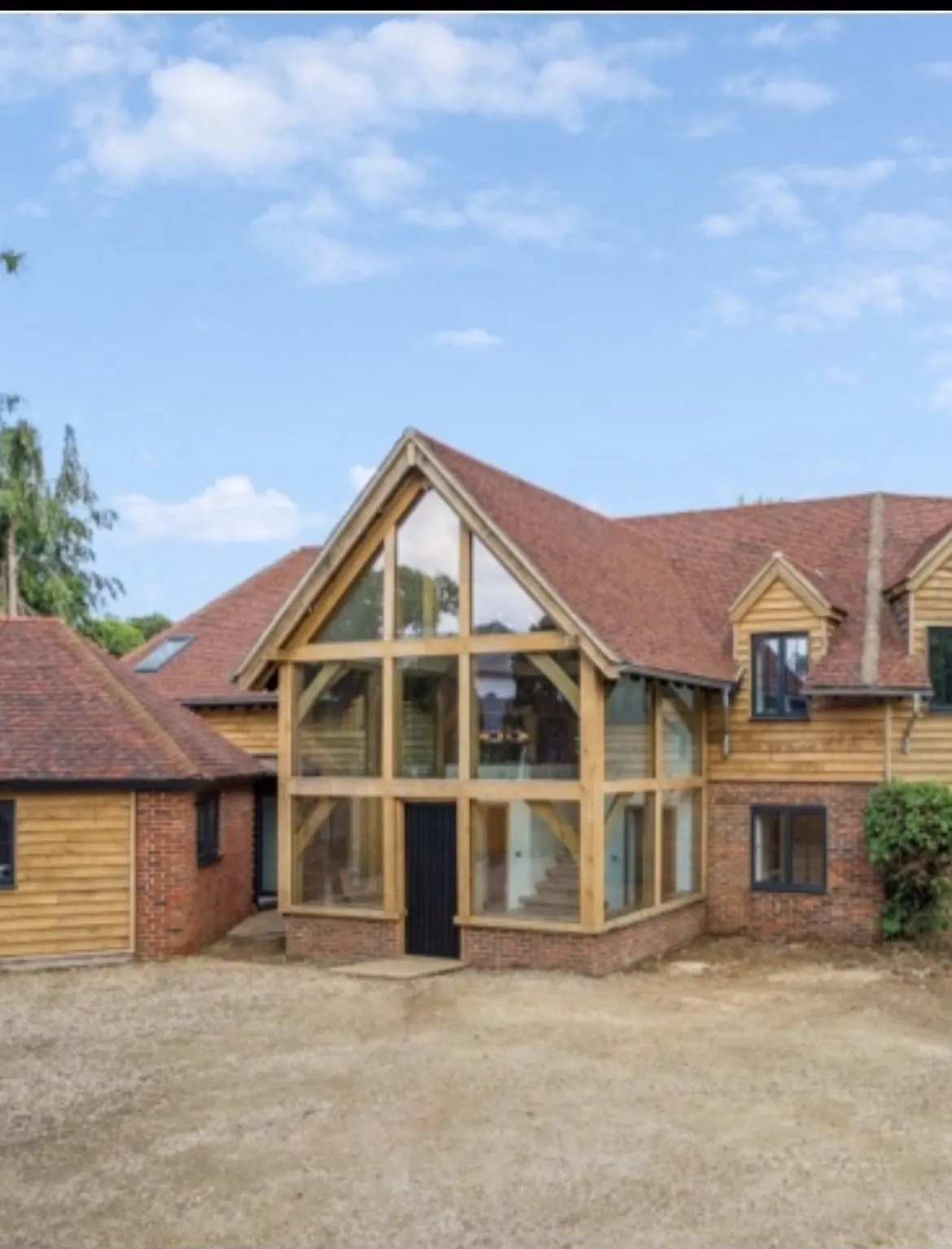 Two-storey glazed oak framed entrance with an oak gable on a brick and oak-clad house