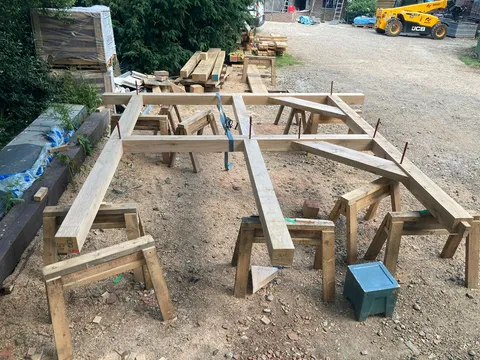 Green oak beams laid out on trestles on site before raising