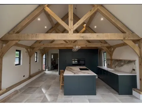 Finished kitchen with exposed oak trusses, an island and bi-fold doors to the garden