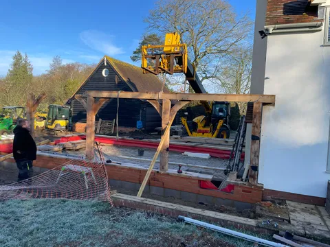 Telehandler lifting oak beams onto a new brick plinth beside the house