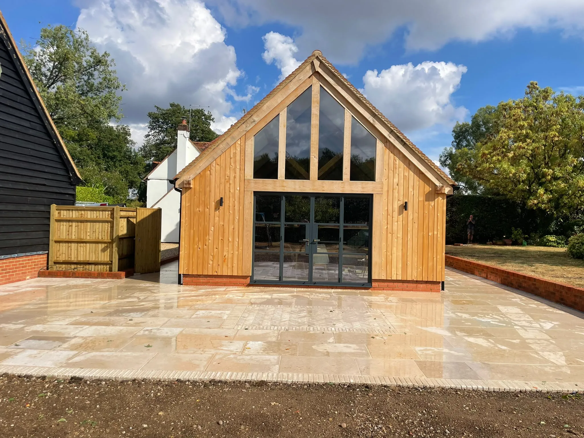 Oak framed extension with a glazed gable and grey doors, built onto a white house with a new patio