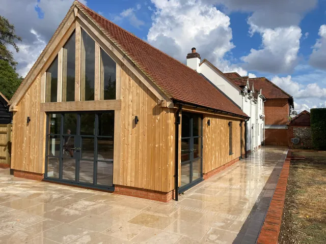 Glazed gable oak framed extension with black-framed doors and a new stone patio