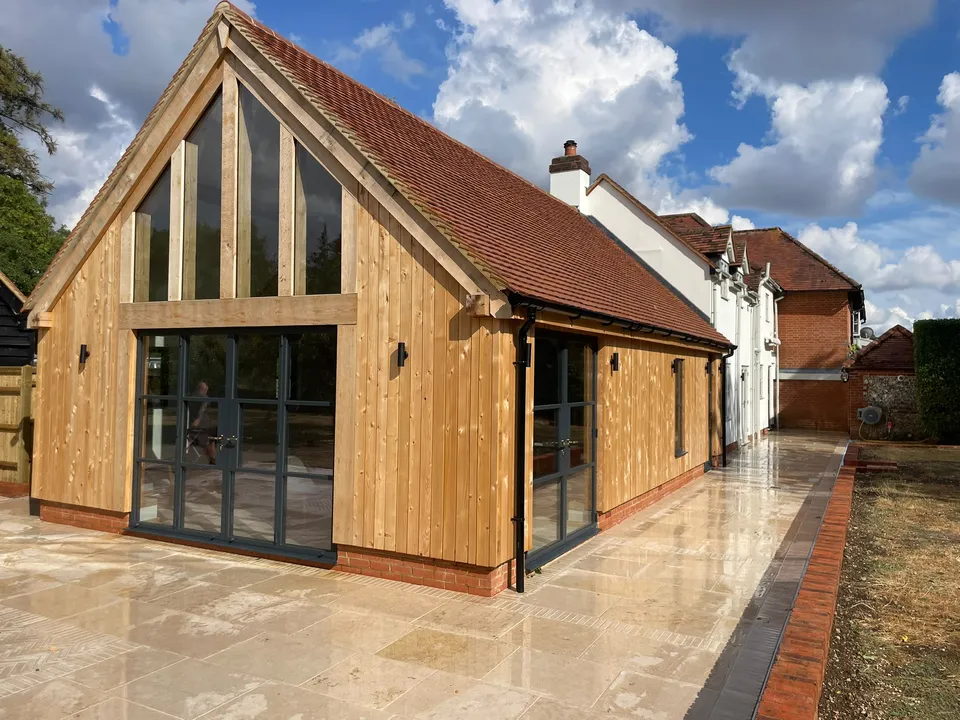 Cowfields kitchen extension: oak framed glazed gable with black-framed doors and a new stone patio