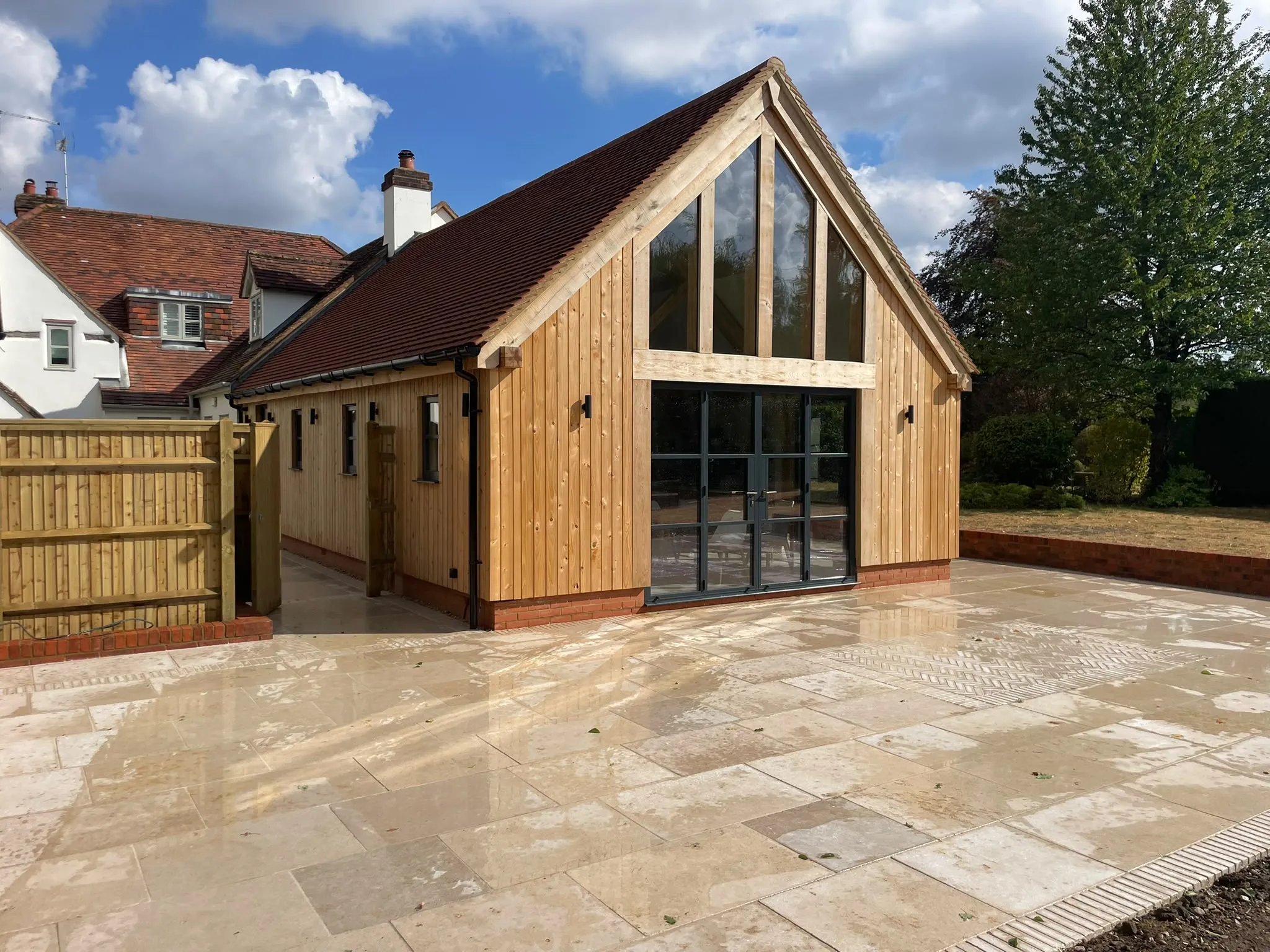 Oak framed extension with a glazed gable and oak cladding, seen from the side across the new patio