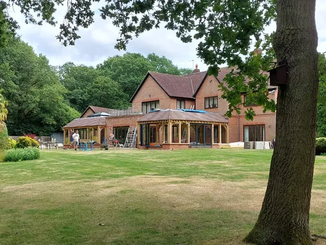 Oak framed garden room seen from the lawn, glazed on three sides at the rear of a brick house