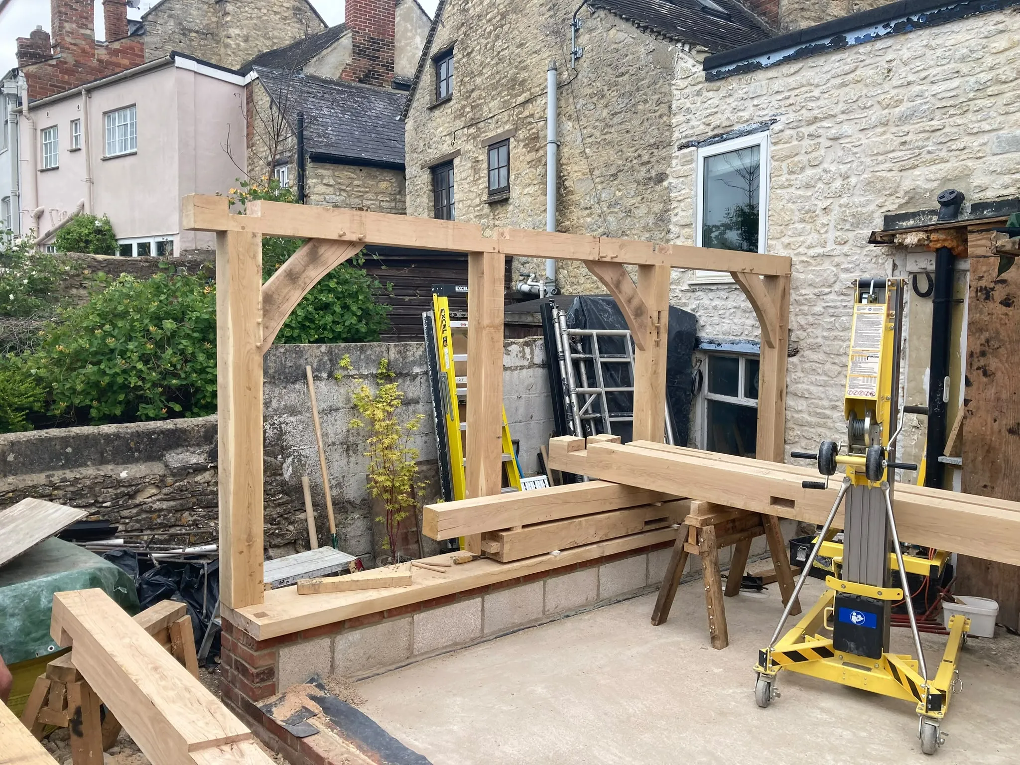 Oak garden room going up on the back of a stone house: the green oak frame raised on its plinth before the flat roof and glazing